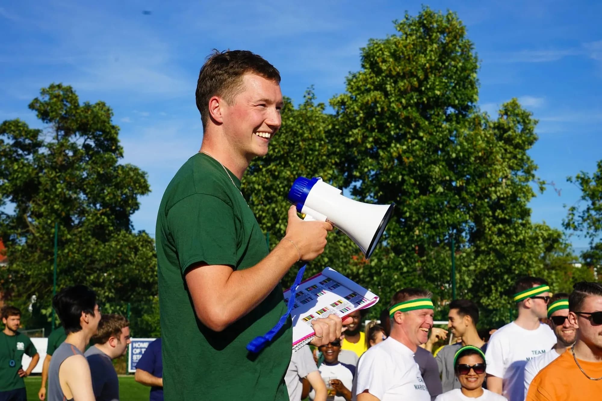 Archie in a green shirt holding a megaphone and a notebook